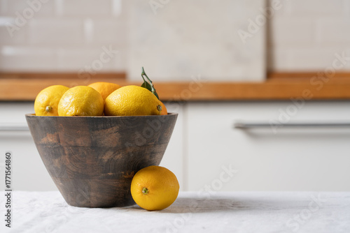 Wooden bowl with yellow lemons on linen tablecloth in bright minimalist kitchen interior