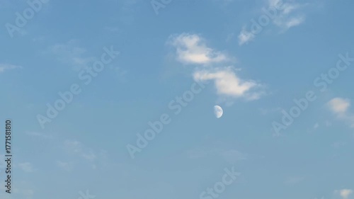 The moon in the sky in daylight The moon at day, A large cloud in the sky. The sky is blue. The cloud is white