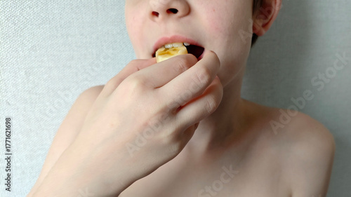 Person eating sliced banana on gray wall background. Kid holding piece of banana in their hand and biting into it. Healthy snack for kids. Child of white race is going to eat round piece of banana