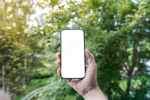 Hand holding a smartphone with a blank white screen in an outdoor natural setting. Perfect for mobile app mockups, UI/UX design presentations, technology advertising, digital marketing