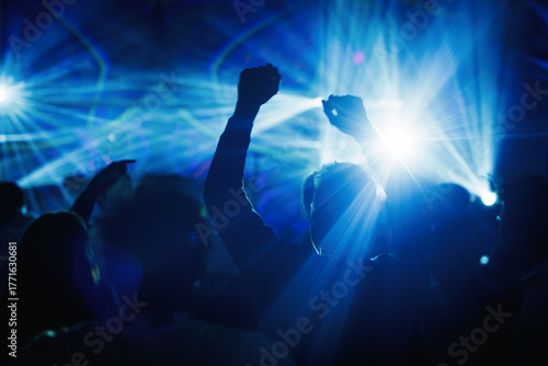 Silhouettes dancing under blue laser lights at concert