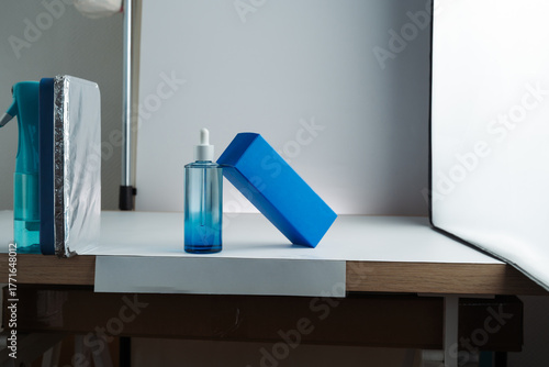 Behind-the-scenes view of product photography setup with softbox, white background, and reflector propped on a spray bottle, mobile photo. Concept of studio, lighting, photography, setup.