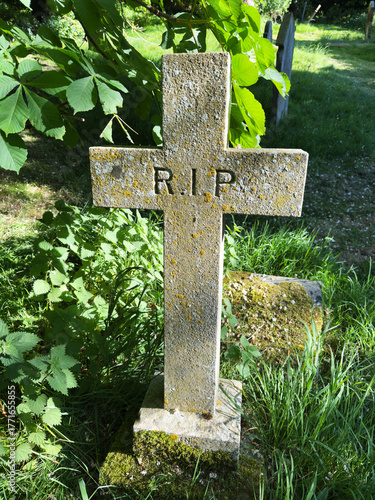 Closeup of an old stone cross in a sunlit cemetery graveyard, bearing the simple inscription, R.I.P.