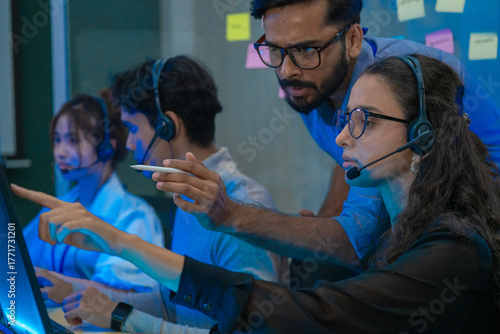 Customer support team in a modern call center receiving guidance from a supervisor. Diverse employees working with headsets and computers, representing teamwork, communication, and business 