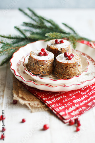 Wallpaper Mural Three mini Christmas puddings decorated with cranberries and sugar powder on white festive plate with fir branches and red napkins over white wooden background. Close up view Torontodigital.ca