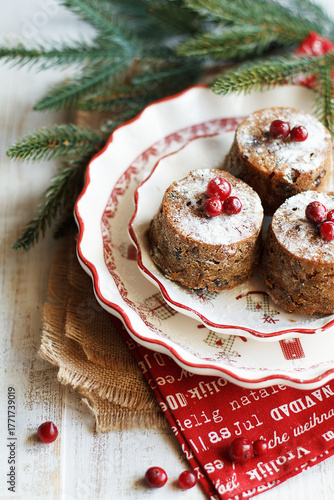 Wallpaper Mural Three mini Christmas puddings decorated with cranberries and sugar powder on white festive plate with fir branches and red napkins over white wooden background. Close up view Torontodigital.ca