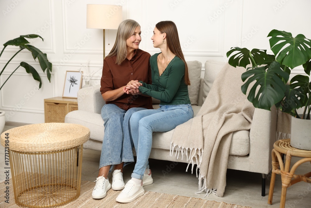 Obraz premium Mother and daughter holding hands on sofa at home