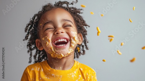 Wallpaper Mural A young Black child is laughing joyfully, covered in peanut butter and macaroni noodles. The child's face is smeared with peanut butter, and noodles are scattered around them. Torontodigital.ca