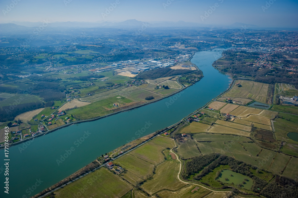 Fototapeta premium This captivating view showcases the Adour river winding through Urt, Landes. Surrounding farmland and peaceful homes highlight the natural beauty of the area, inviting exploration.