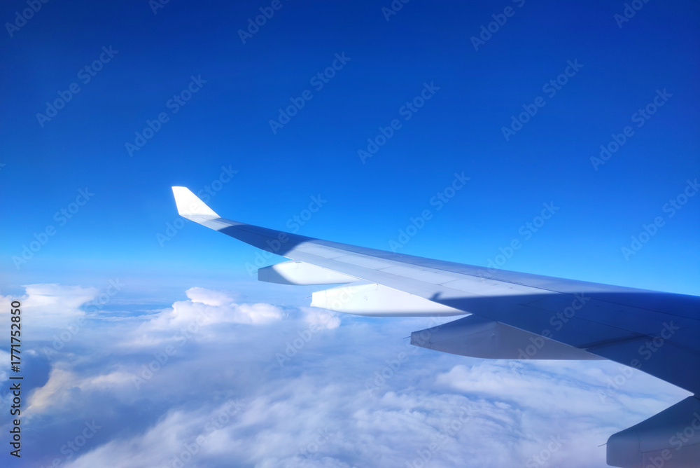 Obraz premium View of airplane wing above clouds on a clear sunny day with blue sky