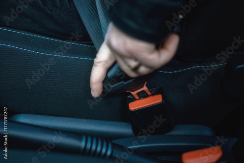 A close-up of a person's hand inserting a seat belt tongue. This is a mandatory action before driving. Suitable for topics such as safety, traffic, regulations, and insurance.