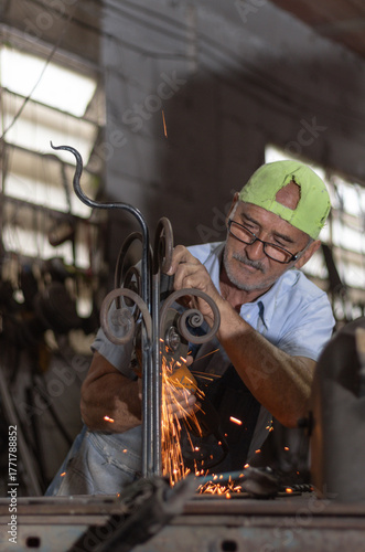 Blacksmith using angle grinder, shaping a decorative wrought iron piece. Sparks illuminate the work, showcasing craftsmanship