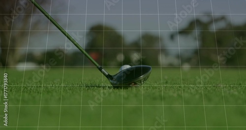 Positioning golf driver head behind golf ball on fairway turf, with tree-lined background