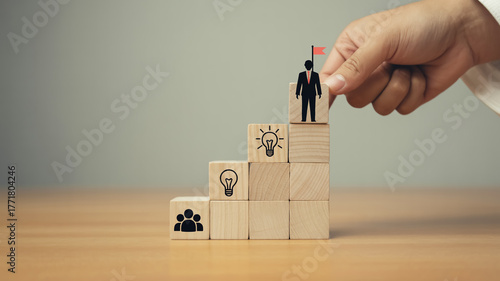 Creative business growth concept with wooden blocks forming upward staircase, teamwork and leadership icons, hand placing final block, symbolizing success, vision, motivation, and strategy.