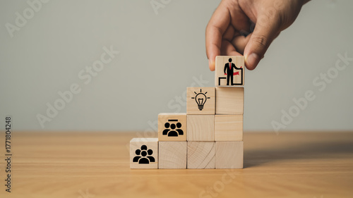 Creative business growth concept with wooden blocks forming upward staircase, teamwork and leadership icons, hand placing final block, symbolizing success, vision, motivation, and strategy.