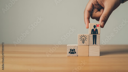 Creative business growth concept with wooden blocks forming upward staircase, teamwork and leadership icons, hand placing final block, symbolizing success, vision, motivation, and strategy.