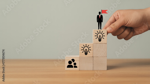 Creative business growth concept with wooden blocks forming upward staircase, teamwork and leadership icons, hand placing final block, symbolizing success, vision, motivation, and strategy.