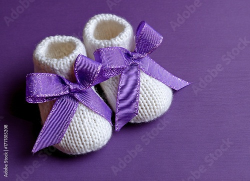 Adorable baby booties adorned with a delicate crowned ribbon, presented artfully on a vibrant purple background, evoking sweetness and new beginnings for charming commercial use.
