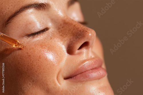 Golden skincare cosmetic serum pouring and flowing from pipette on beautiful female woman beauty models face detail. Gentle natural moisturizing hydration and skin care routine.