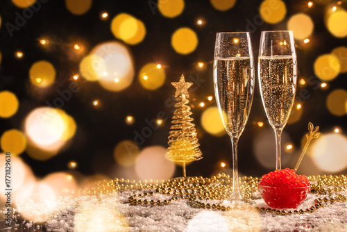 Two glasses of champagne with red caviar on festive golden bokeh background, elegant New Year celebration composition with sparkling wine, Christmas decor and holiday lights, luxury party concept