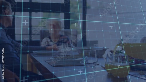 Senior couple seeking connection by window upon translucent tech grid appearing over wooden table