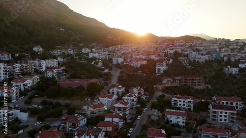Aerial drone video of Kas town at sunrise with sunlight over hills, red rooftops, and calm morning atmosphere. Turkey