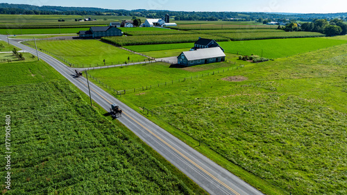 Fotografie Two small vehicles travel along a peaceful country road surrounded by lush green fields and farmhouses