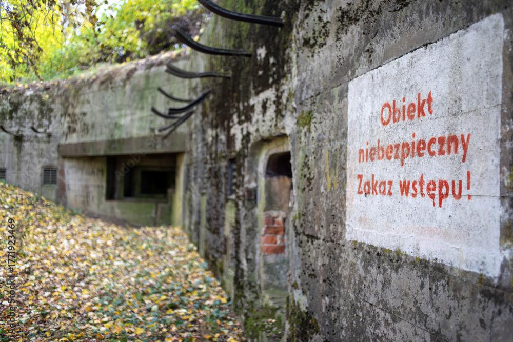 Obraz premium Stary opuszczony betonowy powojenny bunkier stanowiący niebezpieczeństwo podczas eksploracji - na pierwszym planie informacja o zakazie wstępu 