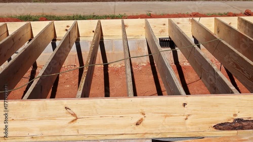 Wooden beams rest on concrete foundation, indicating active construction in residential area.