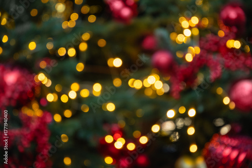 Blurred Christmas tree with red balls and lights garland. Abstract pattern. Defocused background. Xmas holiday spirit.