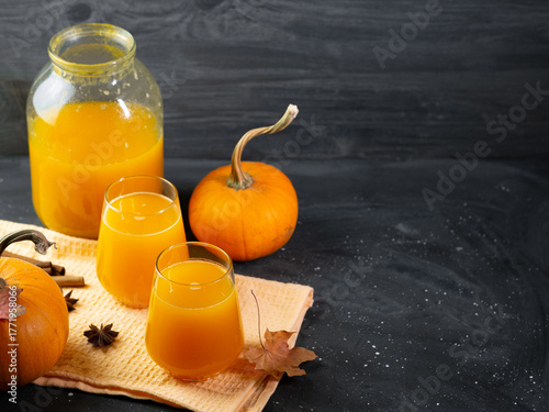 Delicious and healthy homemade pumpkin juice in a glass jar and glasses. Ripe orange pumpkins and spices. Dark background.