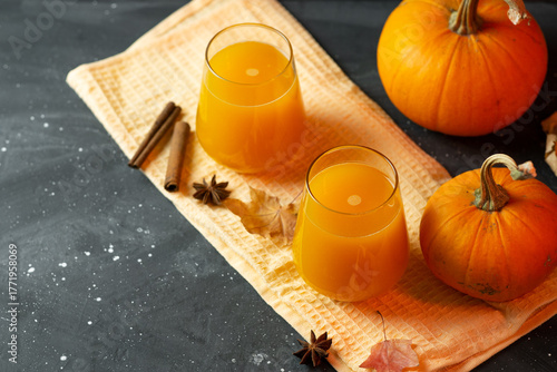 Two glasses of pumpkin juice on a dark table with ripe pumpkins and spices. Top view, copy space. Autumn homemade drink.