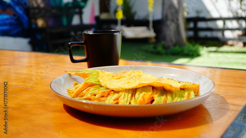 Platillo servido en plato artesanal con una omelette dorada acompañada de flor de calabaza y salsa verde.