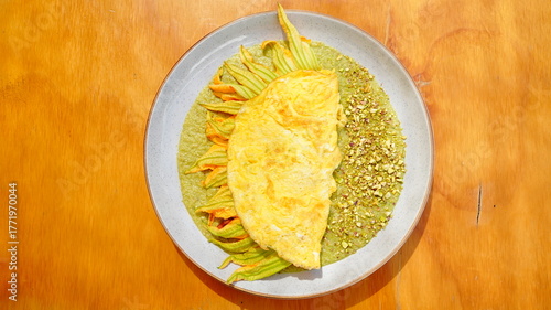 Platillo servido en plato artesanal con una omelette dorada acompañada de flor de calabaza y salsa verde.