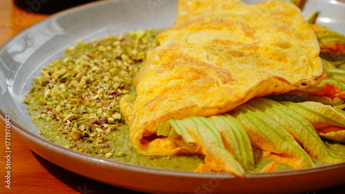 Platillo servido en plato artesanal con una omelette dorada acompañada de flor de calabaza y salsa verde.