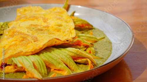 Platillo servido en plato artesanal con una omelette dorada acompañada de flor de calabaza y salsa verde.