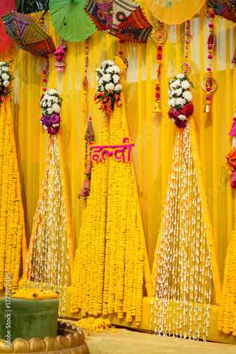 Indian haldi ceremony backdrop decorated with yellow marigold garlands, floral arrangements, and colorful umbrellas representing Indian wedding traditions and festive celebration.