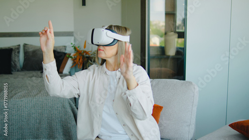 Elderly woman experiences virtual reality in a modern living room, engaging with immersive content while seated on a cozy sofa