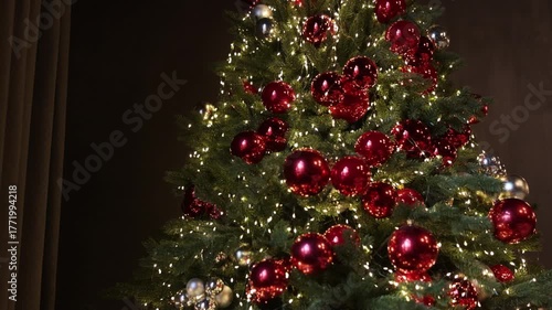 Christmas tree, elegant decor, cozy atmosphere. Beautifully decorated Christmas tree featuring red and silver baubles, warm white string lights, and dense green branches in dark room.