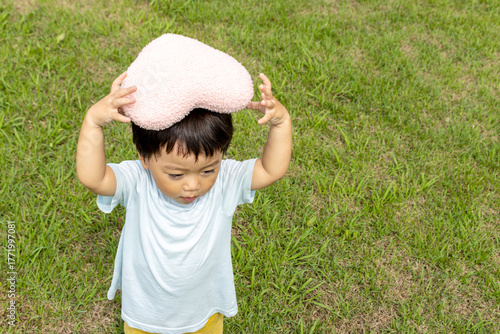ハートのクッションを持って草原に立つ男の子（2歳、日本人）