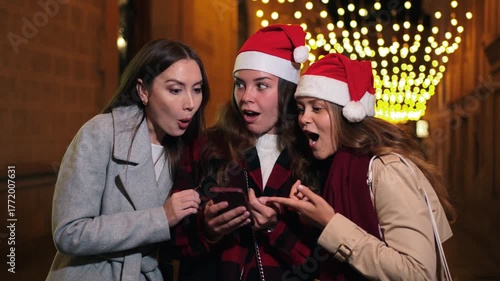 A joyful group of friends engaged in searching for gifts on their smartphone, sharing excitement during the festive Christmas night celebration, capturing the spirit of friendship and holiday cheer.