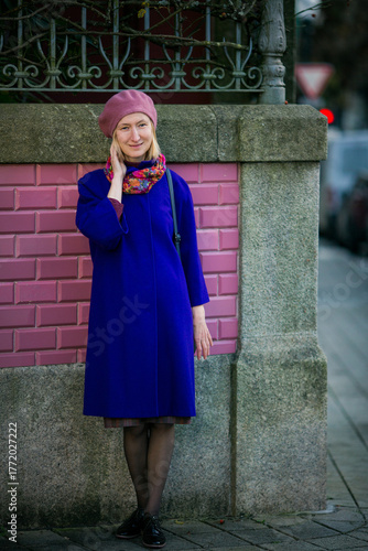 A woman in a deep blue coat and a dusty rose beret stands by a wall with rose-colored tiles in Porto, Portugal. The scene feels elegant, balanced, and full of quiet charm.