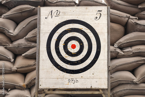 A traditional shooting target with black rings and a bullseye, placed against a sandbag wall.