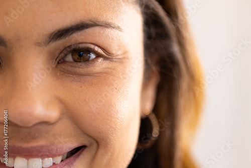 Smiling woman revealing white teeth inside bright room wearing gold hoop earring