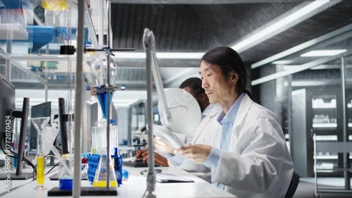 Clinical microbiologist uses laboratory lamp to examine liquid in test tube for clarity and color changes. Senior lab employee holds test tube to light source for impurity detection, camera A