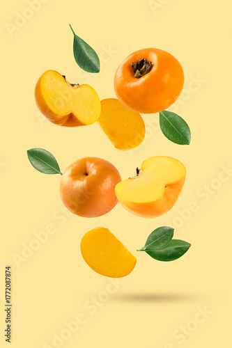 Falling persimmon fruits with sliced and leaves isolated on yellow background.