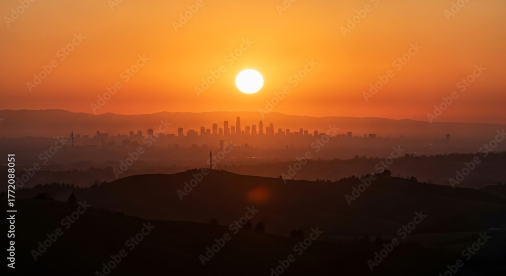 Fototapeta premium Vibrant urban skyline silhouette at sunrise with orange sky and hills in foreground panorama