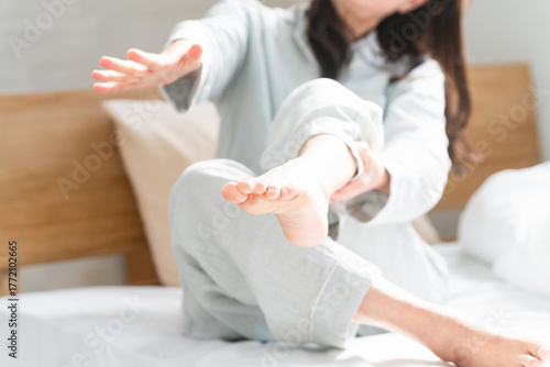 起きてベッドの上で足が攣る女性