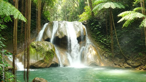 Scenic Waterfall Cascading into Emerald Pool Surrounded by Lush Green Tropical Forest with Sunlight Filtering Through Canopy on a Bright Day