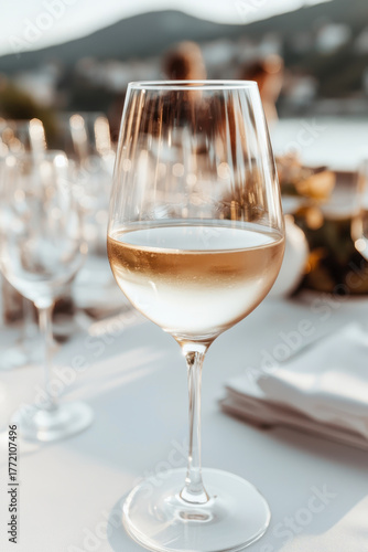 White wine glass on table at outdoor dinner party overlooking coastal view with soft golden light and elegant table setting